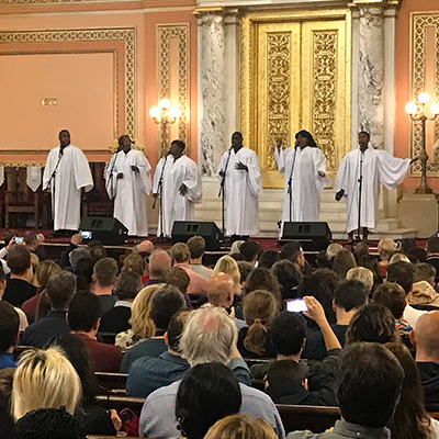 Gospel group wearing striking white robes singing to a church full of people